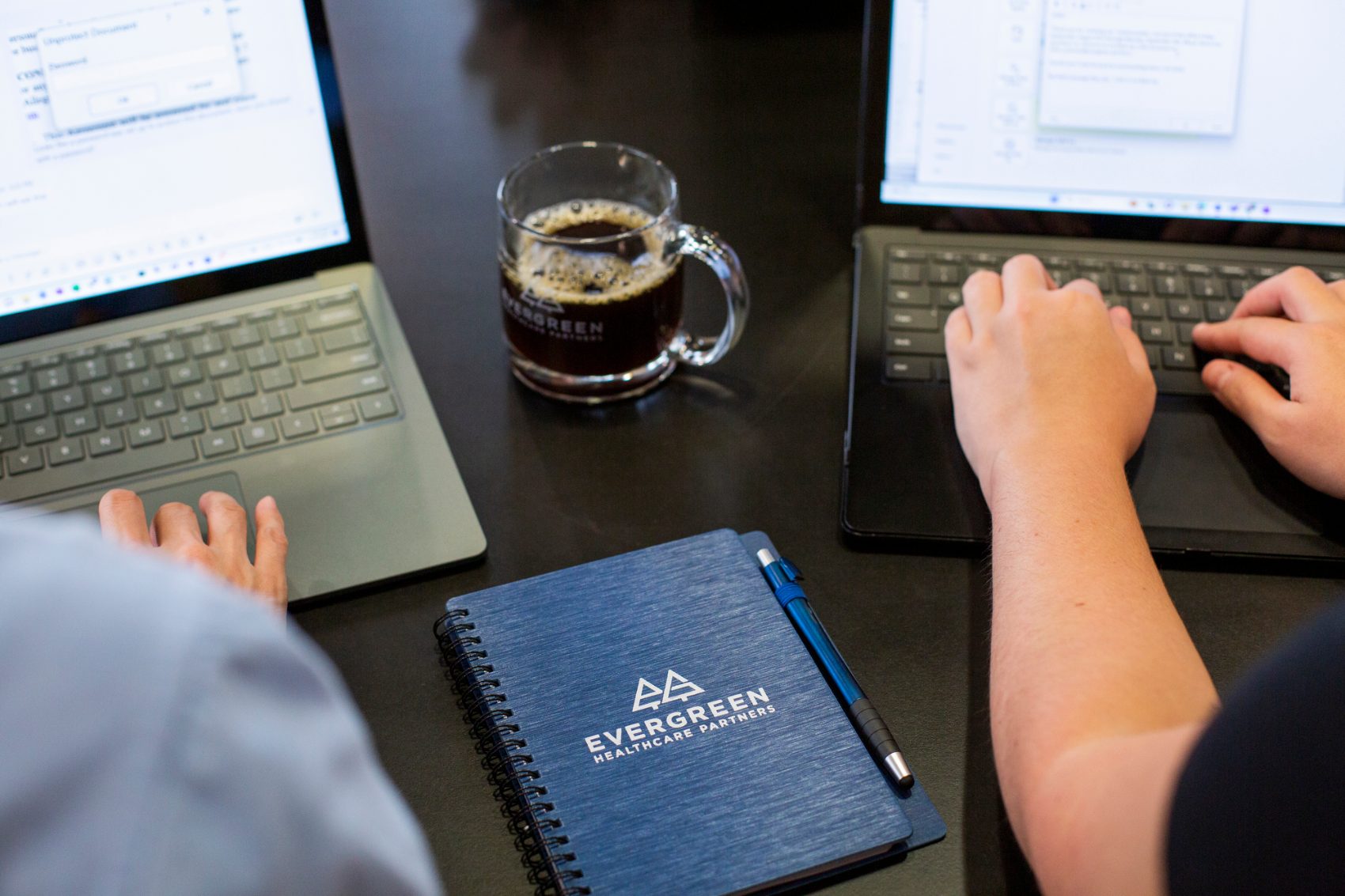 Evergreen consultant reviewing work on a laptop with a branded notebook and mug